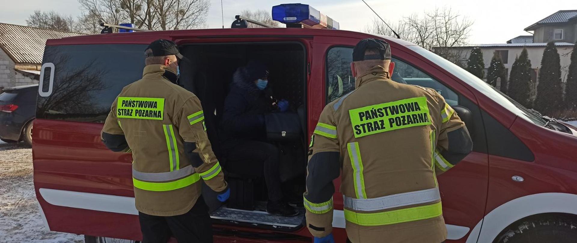 Zdjęcie przedstawia dwóch strażaków na tle wozu PSP. 