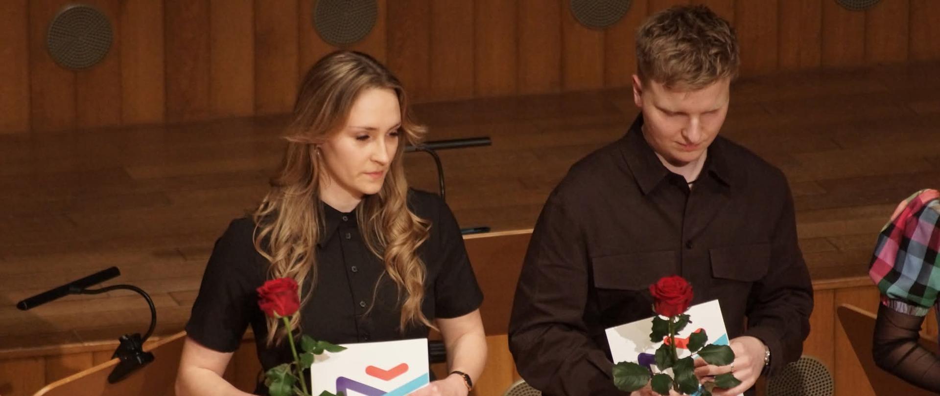 Absolwenci ZPSM trzymają w ręku róże i dyplomy, na tle podestów drewnianych