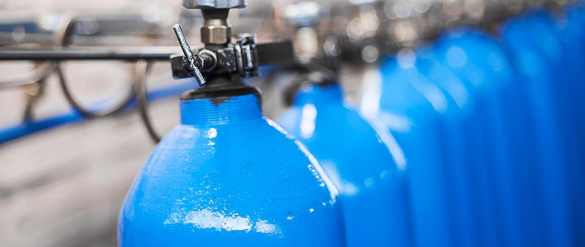 Zdjęcie przedstawia butle z tlenem w kolorze niebieskim. Są one ustawione w rzędzie.