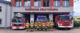 Na zdjęciu strażacy na tle samochodów pożarniczych oraz remizy