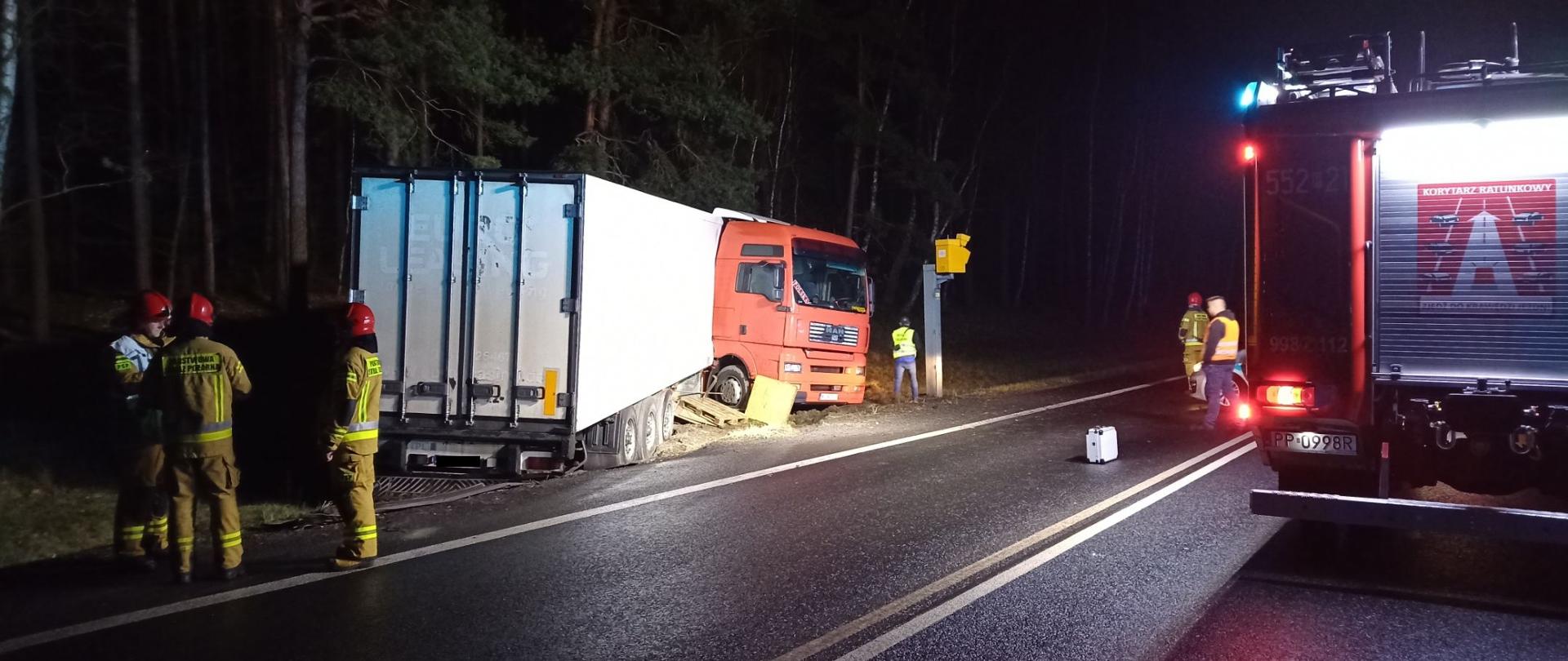 Na zdjęciu widać stojący poza drogą, uszkodzony samochód ciężarowy oraz strażaków.
