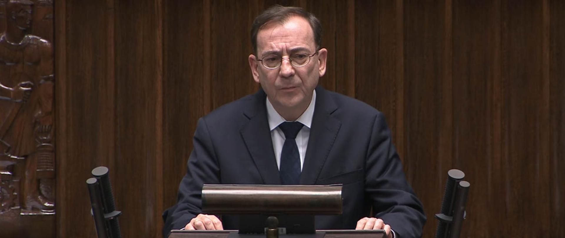 Na zdjęciu widać stojącego i przemawiającego z mównicy sejmowej ministra Mariusza Kamińskiego.