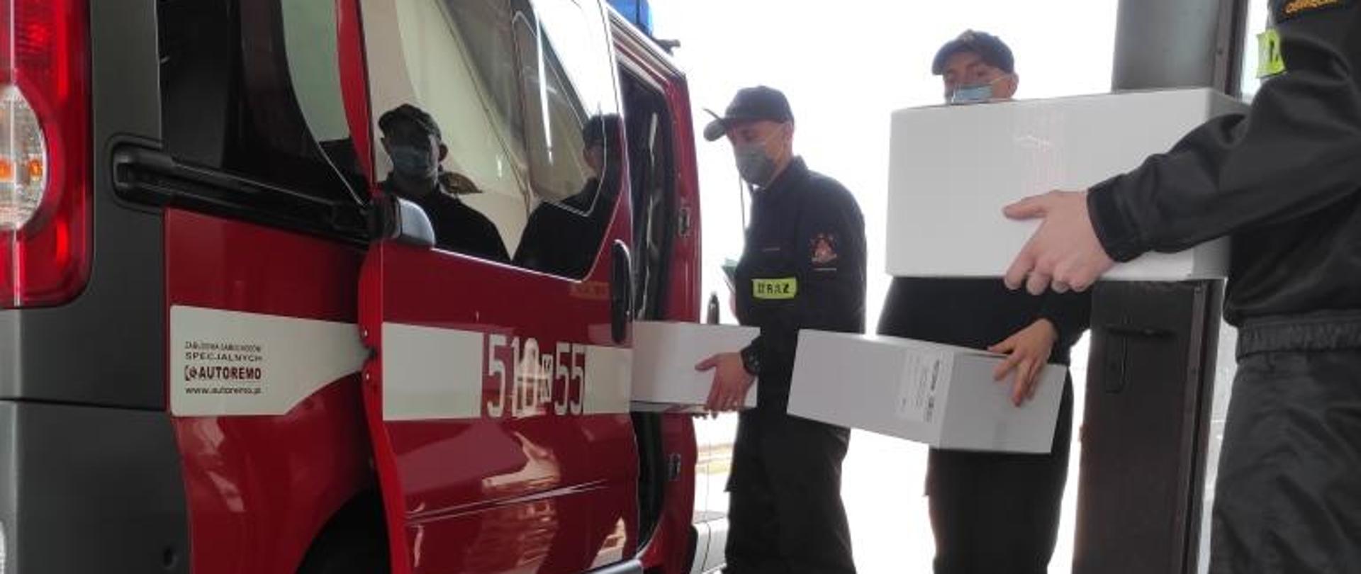 Strażacy wkładający do samochodu pożarniczego środki ochrony