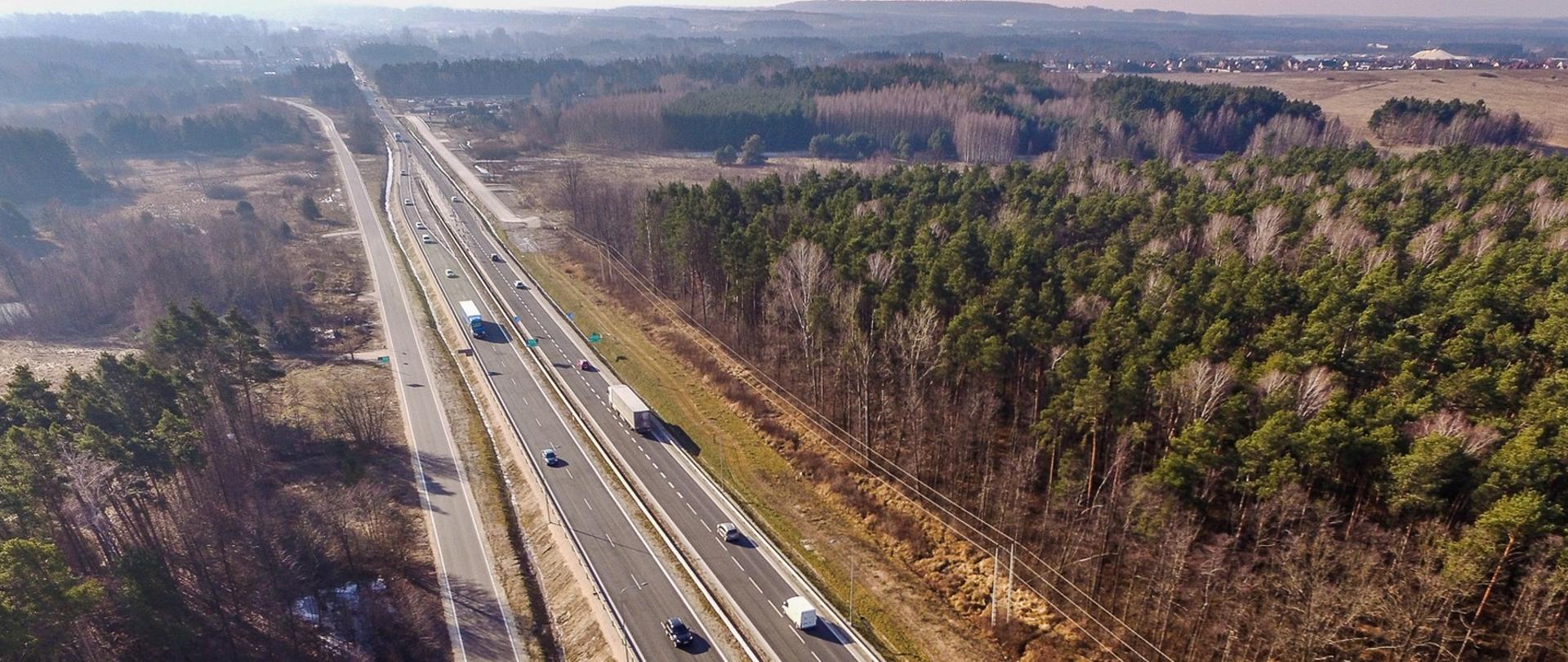 DK73 obwodnica Morawicy etap I - zdjęcie z drona przedstawia dwujezdniową drogę główną z równolegle biegnącą drogą dojazdową, przy drodze drzewa, w oddali dwie jezdnie schodzą się w jedną