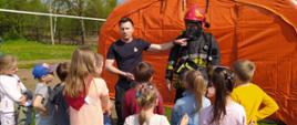 Na zdjęciu strażacy prezentują dzieciom elementy ubrania strażaka