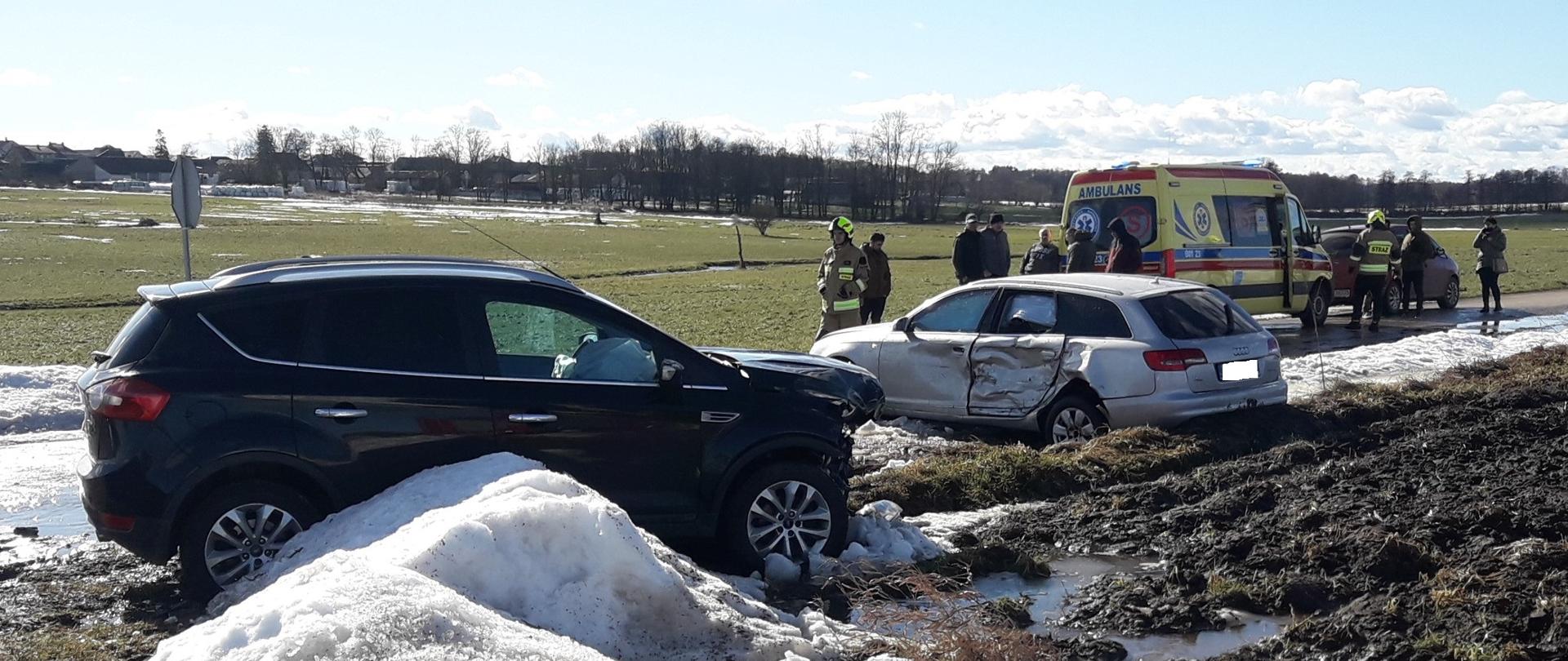 Uszkodzone dwa samochody osobowe. W tle karetka pogotowia i strażacy OSP.