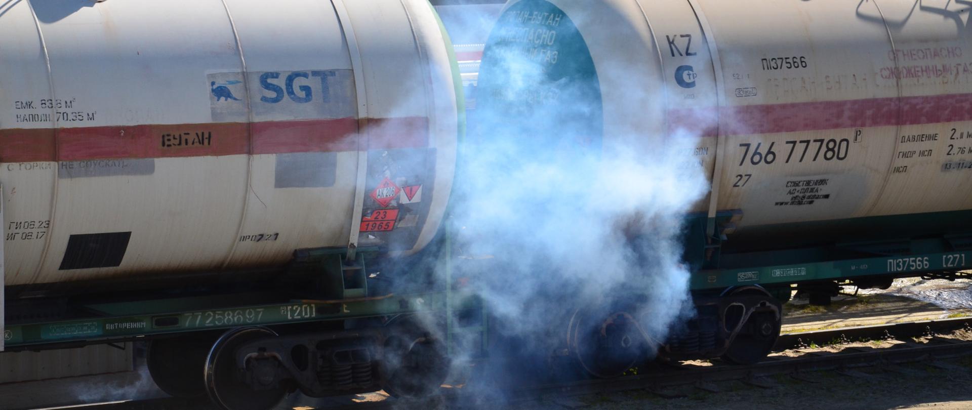 Na zdjęciu cysterny kolejowe z gazem pomiędzy którymi wydobywa się dym.