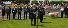 XI Powiatowe Zawody Sportowo-Pożarnicze OSP i MDP. Stadion w Miejskiej Górce. Na tle gości i trybun, na których zasiadają kibice, do zebranych przemawia komendant powiatowy PSP w Rawiczu. Z prawej strony znajduje się biały stół.