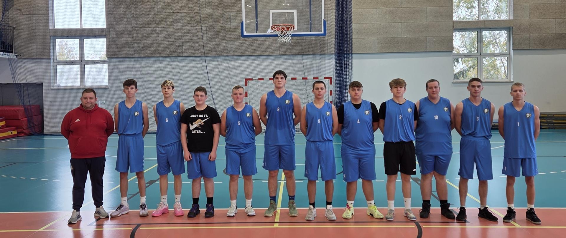 Grupa młodych zawodników z trenerem w hali sportowej.