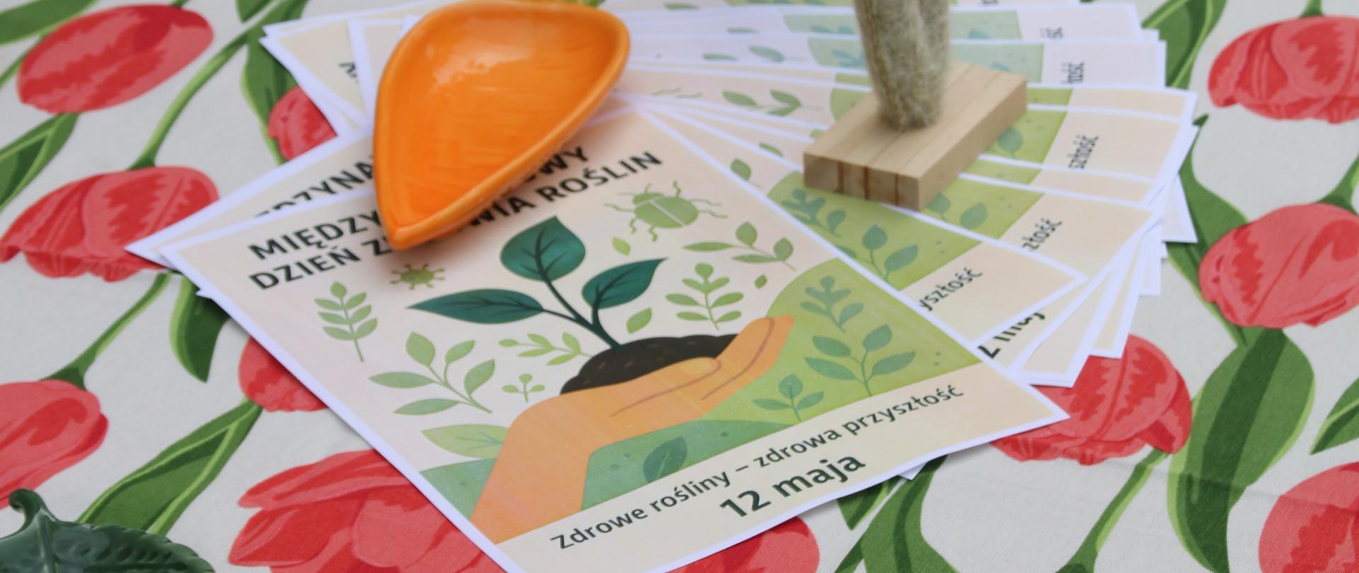 Stół z obrusem w tulipany, na nim ulotka "Międzynarodowy Dzień Zdrowia Roślin"