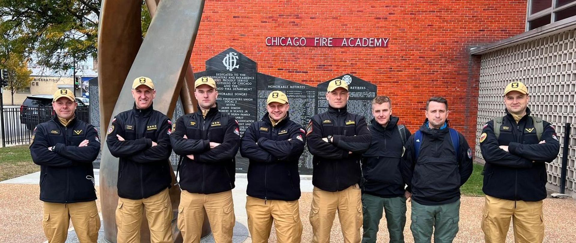 Polska delegacja (8 mężczyzn) pozuje do zdjęcia na tle budynku Chicago Fire Academy