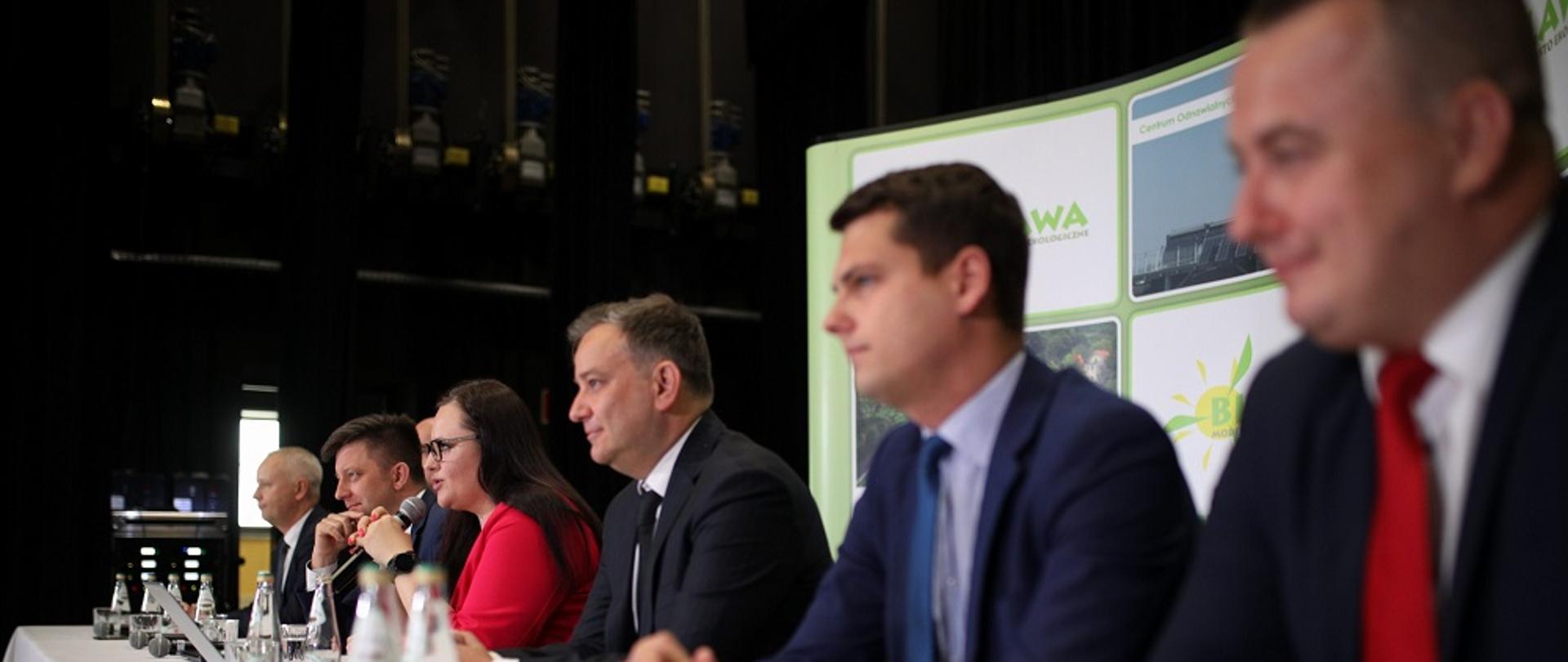 Przy stole konferencyjnym siedzą od prawej: senator Aleksander Szwed, wicemarszałek województwa Grzegorz Maćko, poseł Marcin Gwóźdź, minister Małgorzata Jarosińska-Jedynak, minister Michał Dworczyk oraz przedstawiciel lokalnych samorządowców.