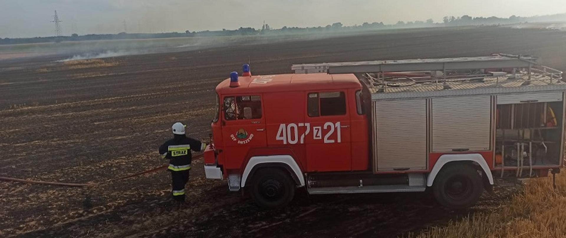 Przedstawia pożar ścierniska i akcję gaśniczą w miejscowości Daszewo. Na pierwszym planie samochód strażacki z OSP w Daszewie oraz strażak w ubraniu specjalnym
