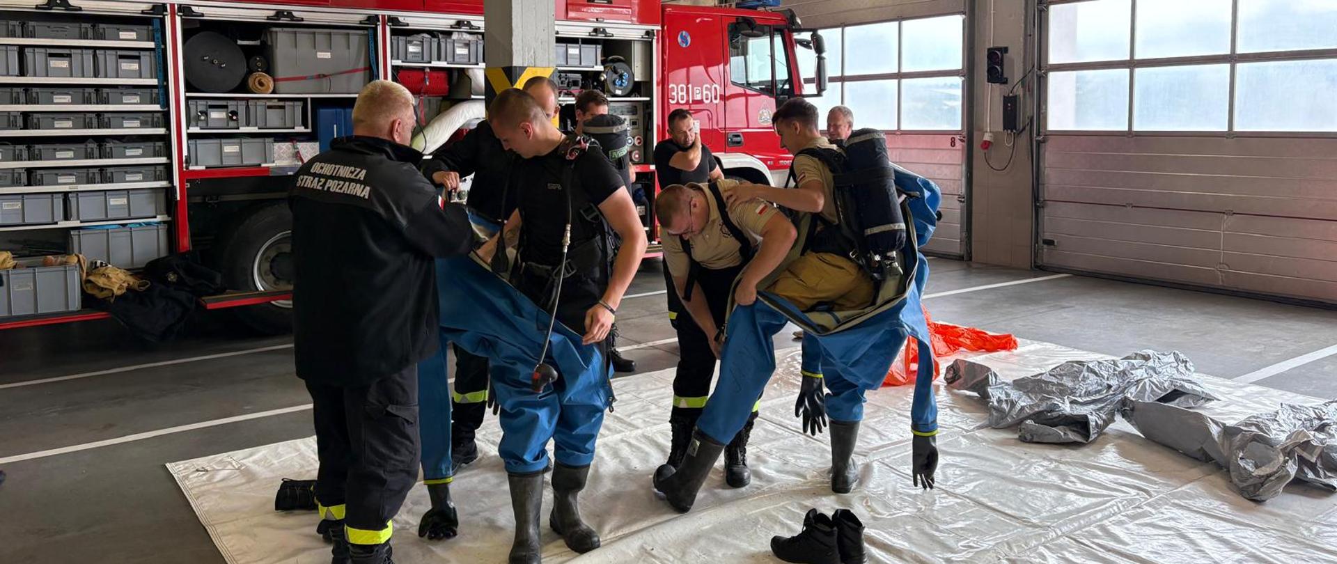 Strażacy zakładają kombinezony chemiczne.