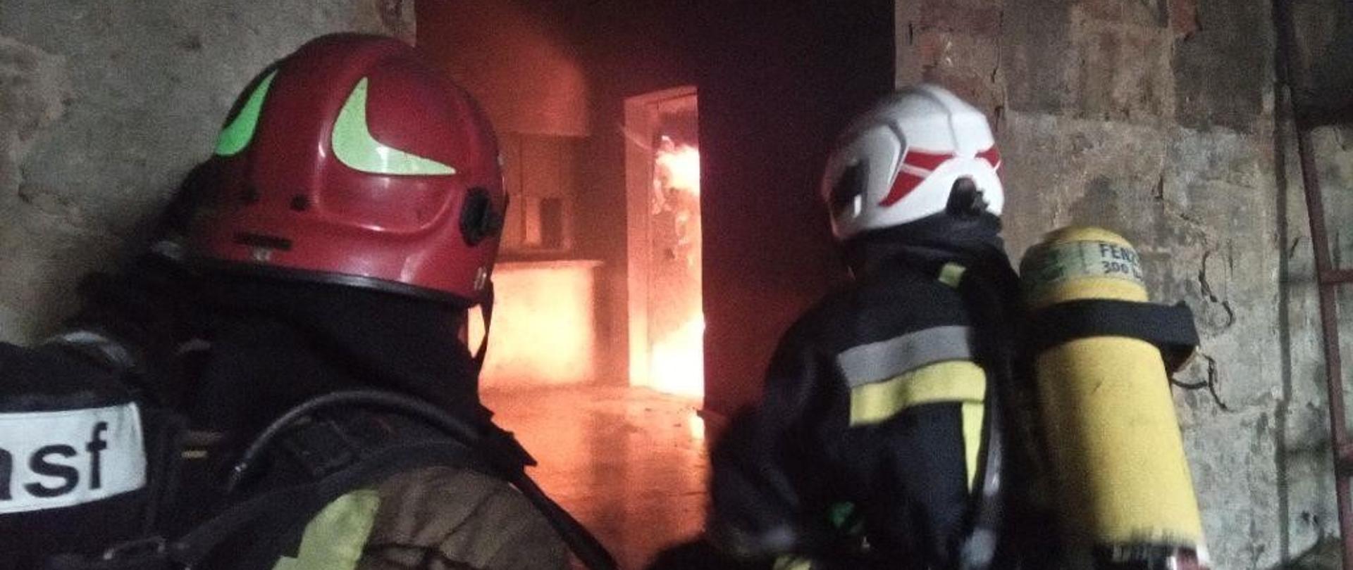 Strażacy wchodzący do płonącego pomieszczenia.