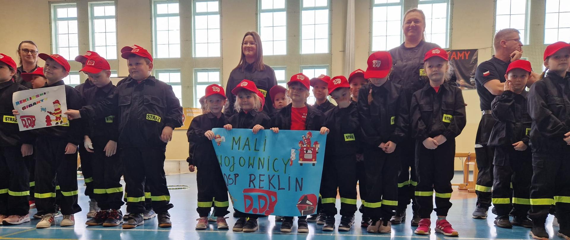 Na zdjęciu w dwuszeregu ustawieni uczestnicy olimpiady, ubrani w ubrania koszarowe. Za dziećmi stoją opiekunowie. 