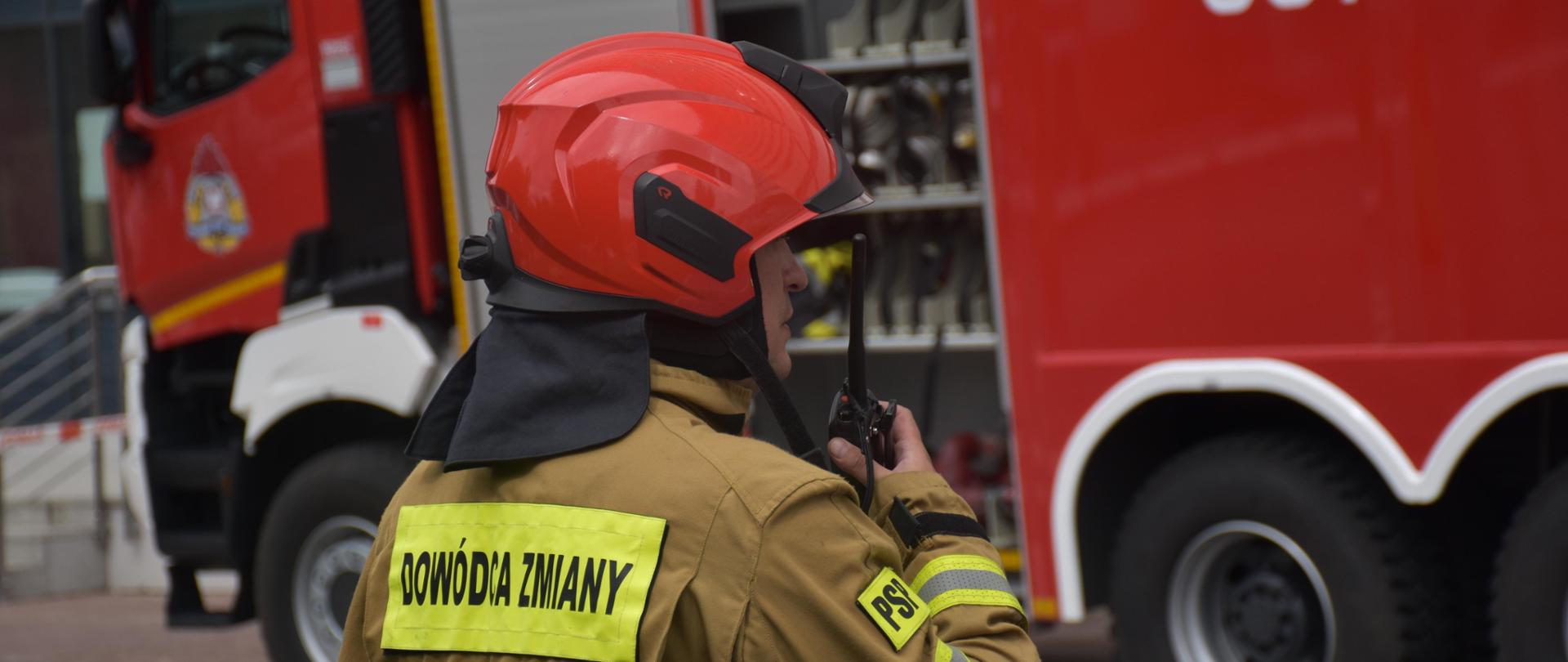 Strażak z radiotelefonem w ręku, w tle samochód pożarniczy