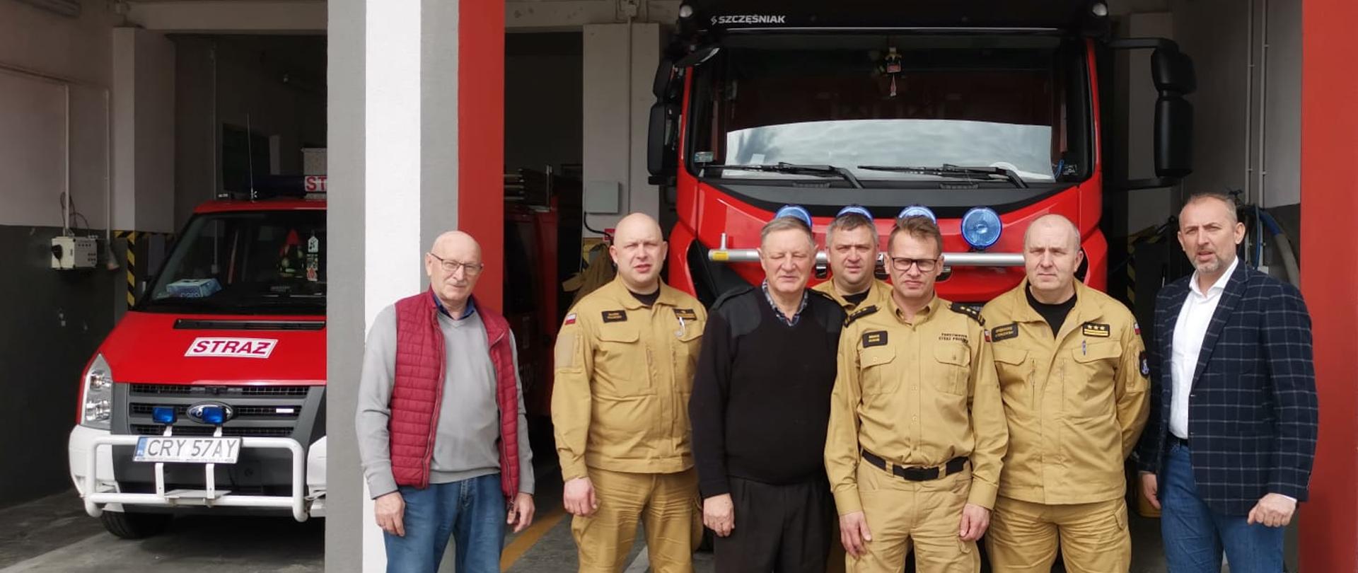 Przed wjazdem do remizy Ochotniczej Straży Pożarnej w Skrwilnie stoją trzej druhowie, Zastępca Kujawsko-Pomorskiego Komendanta Wojewódzkiego Państwowej Straży Pożarnej starszy brygadier Marek Rusoń, kujawsko-pomorski koordynator ratownictwa medycznego Państwowej Straży Pożarnej młodszy brygadier Marek Ruciński, Komendant Powiatowy Państwowej Straży Pożarnej w Rypinie starszy brygadier Grzegorz Łydkowski oraz Dowódca Jednostki Ratowniczo-gaśniczej Państwowej Straży Pożarnej w Rypinie - brygadier Dariusz Łęgosz. Spotkanie to było wizytacją Zastępcy Kujawsko-Pomorskiego Komendanta Wojewódzkiego Państwowej Straży Pożarnej starszego brygadiera Marka Rusonia w jednostkach Ochotniczych Straży Pożarnych będących w Krajowym systemie ratowniczo-gaśniczym powiatu rypińskiego. W tle dwa samochody pożarnicze.