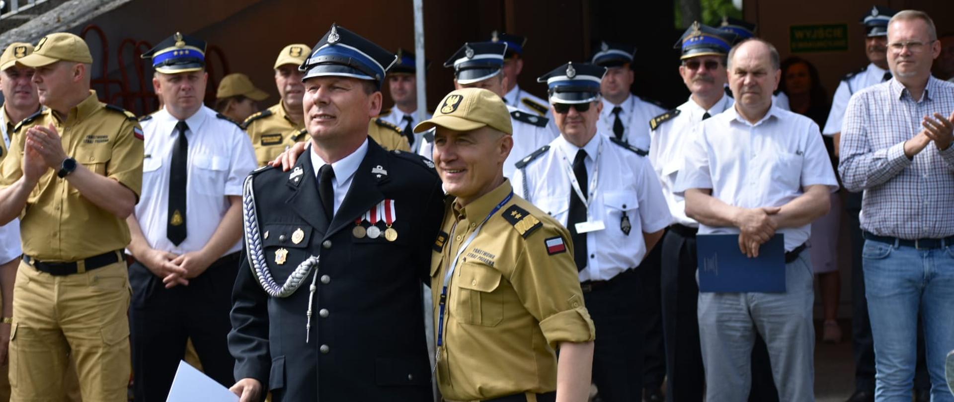 zdjęcie komendanta z druhem osp w tle duża grupa strażaków