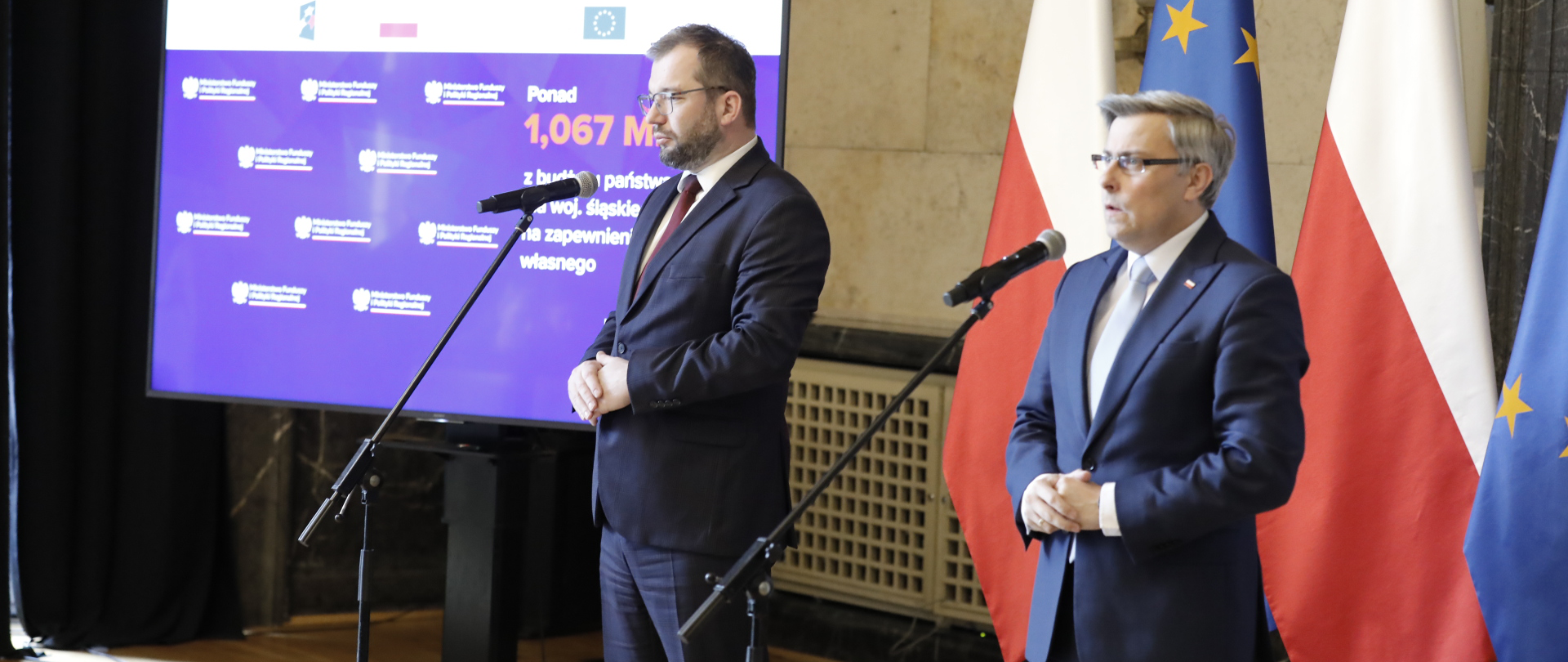 Minister Grzegorz Puda i wojewoda Jarosław Wieczorek przed mikrofonami. Za nimi flagi PL i UE oraz ekran.