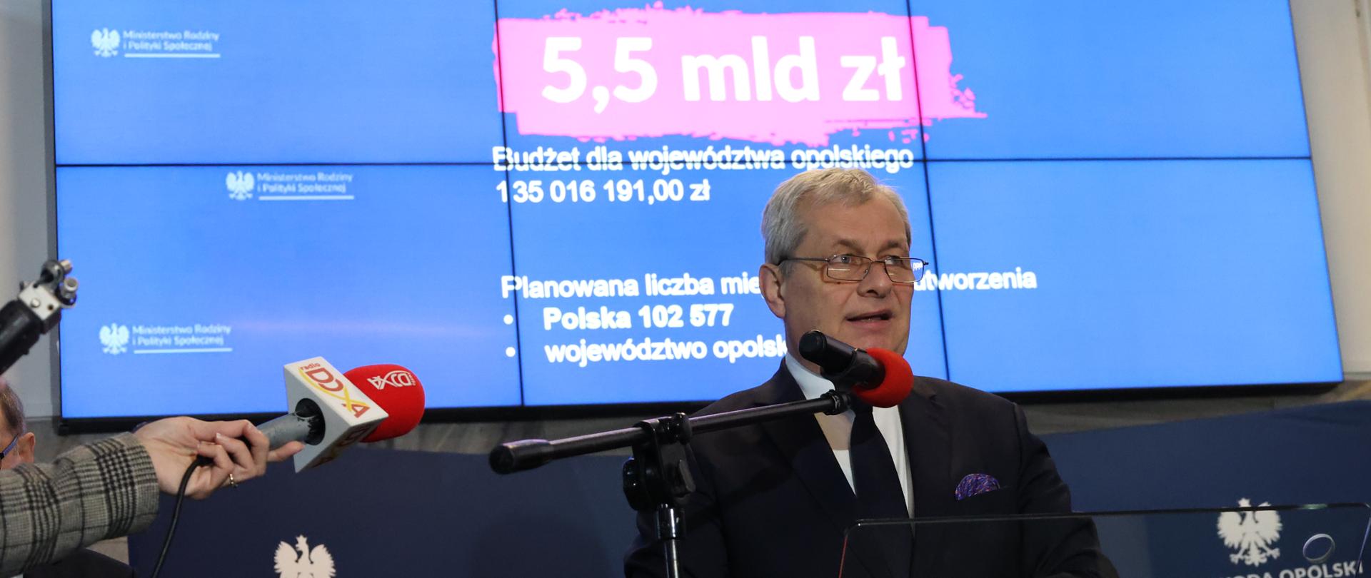 Na tle ścianki stoi przed mikrofonem Wojewoda Opolski 