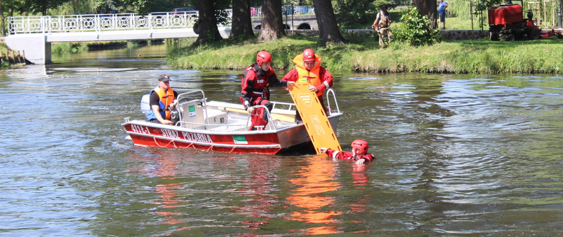 Zdjęcie przedstawia ratowników na łodzi motorowej podczas ratowania poszkodowanego z wody za pomocą deski ortopedycznej
