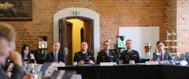Prezydium posiedzenia siedzi przy stole konferencyjnym. Wśród uczestników są funkcjonariusze Państwowej Straży Pożarnej oraz przedstawiciele administracji.