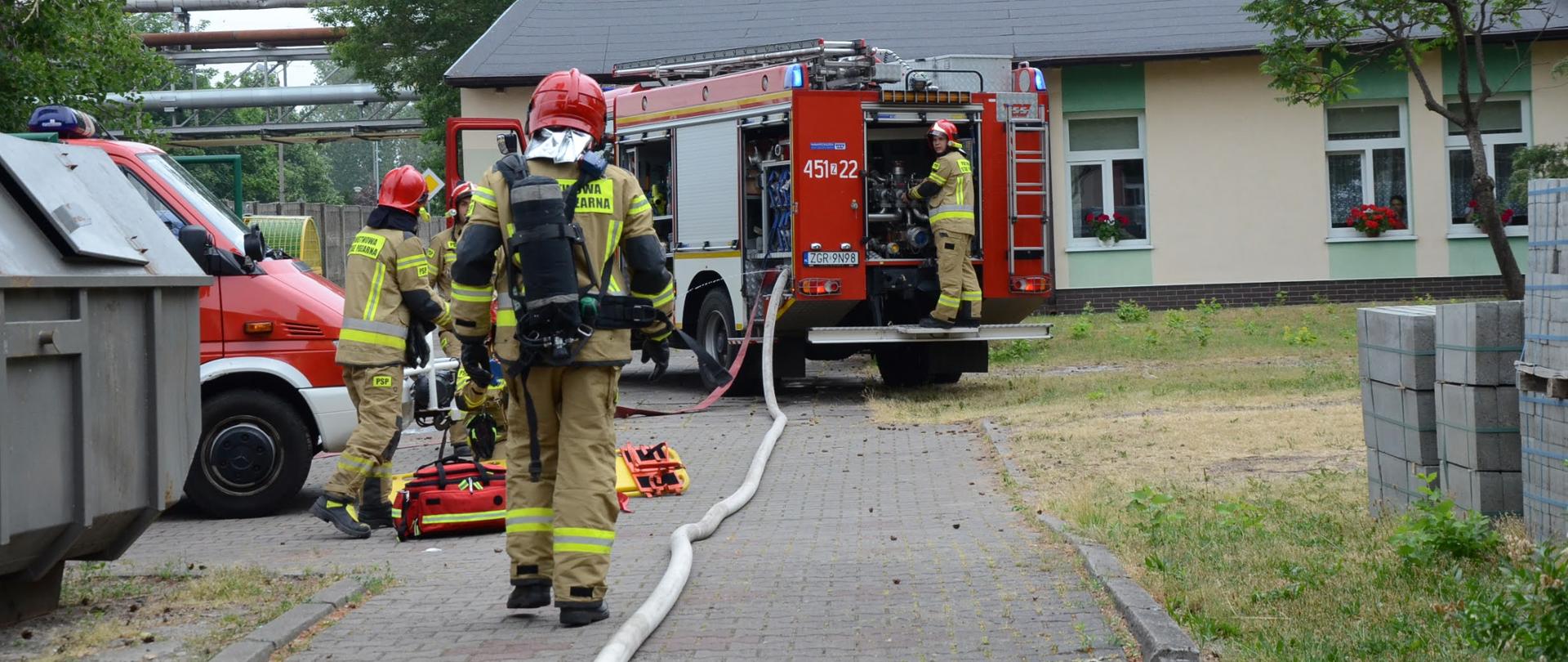 Zdjęcie przedstawia strażaków podczas działań, w tle samochody strażackie