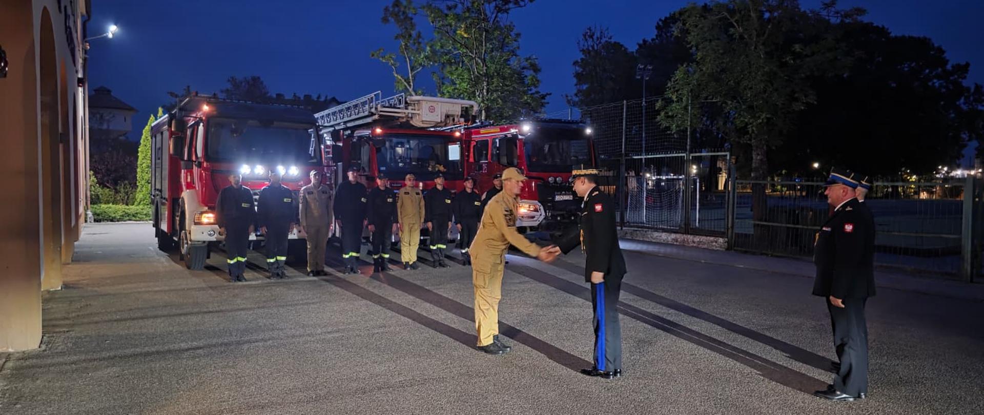 Złożenie meldunku Komendantowi Głównemu przez Dowódcę zmiany. W tle w szyku stoją kartuscy strażacy