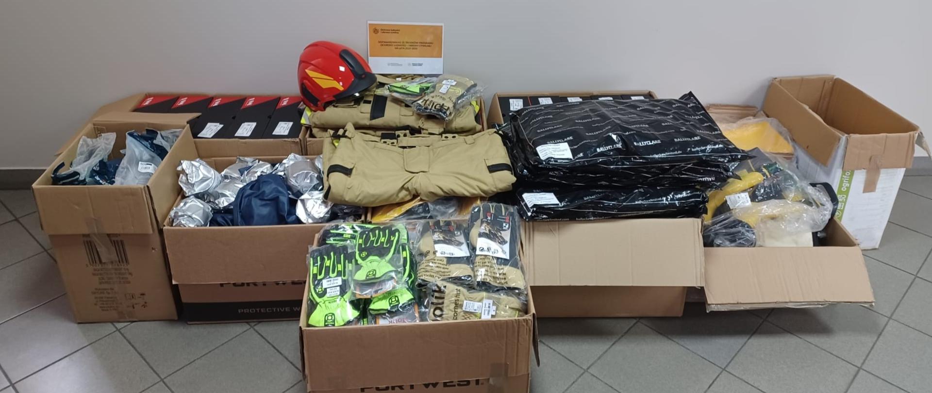 Fotografia przedstawia zakupione elementy umundurowania i wyposażenia osobistego strażaków. Asortyment w kartonach, fabrycznie zapakowany.