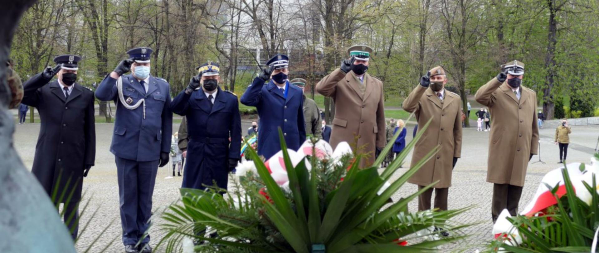 Na zdjęciu widoczna jest delegacja służb mundurowych, stojąca w szeregu i salutująca przed pomnikiem Powstańców Śląskich w Katowicach w czasie uroczystości obchodów rocznicy uchwalenia Konstytucji 3 Maja i 100. rocznicy wybuchu III Powstania Śląskiego.