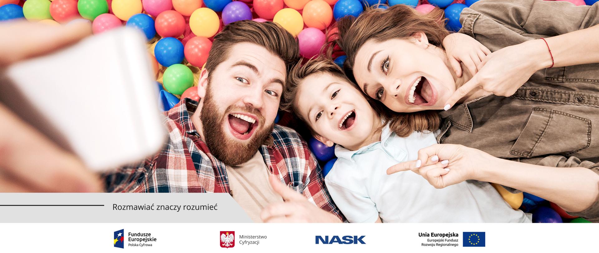 Leżący na kolorowych kulkach uśmiechnięci rodzice i dziecko robią sobie selfie,