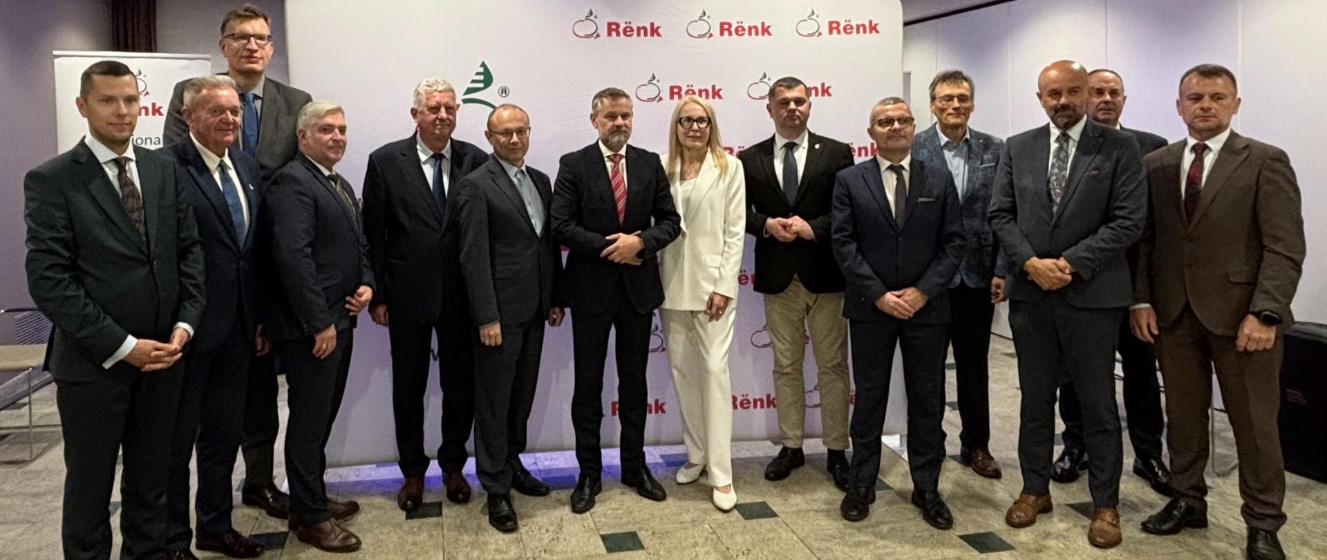 Wiceminister Grzegorz Wrona i inni uczestnicy wydarzenia na tle ścianki. 