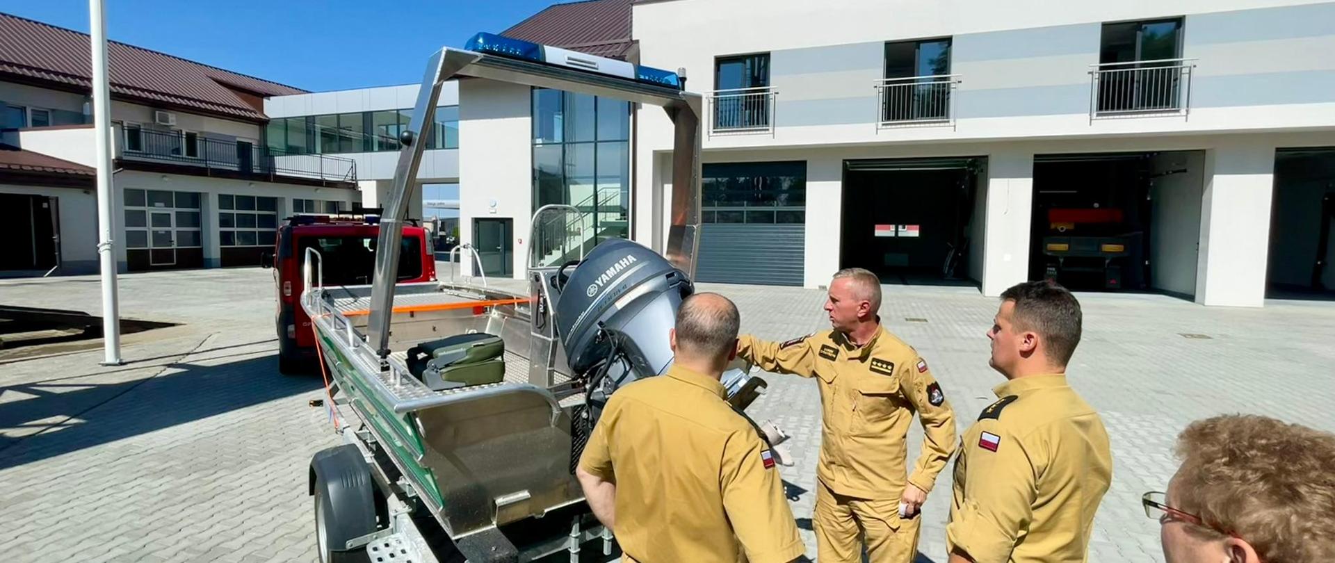 Zdjęcie przedstawia łódź ratowniczą na przyczepce. w Tle widoczni strażacy oraz osoby cywilne.