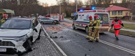 Rozbite 2 samochody osobowe na DK 55, na drodze stoją strażacy oraz ratownik medyczny, w tle samochód strażacki i karetka pogotowia