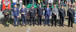 Zdjęcie przedstawia mężczyzn (w tym m.in Sekretarz Stanu w Kancelarii Prezesa Rady Ministrów, Burmistrza Krobi oraz przedstawiciela Komendanta Powiatowego PSP w Gostyniu) podczas uroczystego zakończenia zawodów. Stoją oni w szeregu. W tle pozostali uczestnicy zawodów stoją na trybunach stadionu.