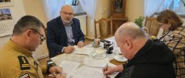 Przedstawiciele Państwowej Straży Pożarnej i innych instytucji podpisują dokumenty podczas spotkania roboczego przy stole konferencyjnym.