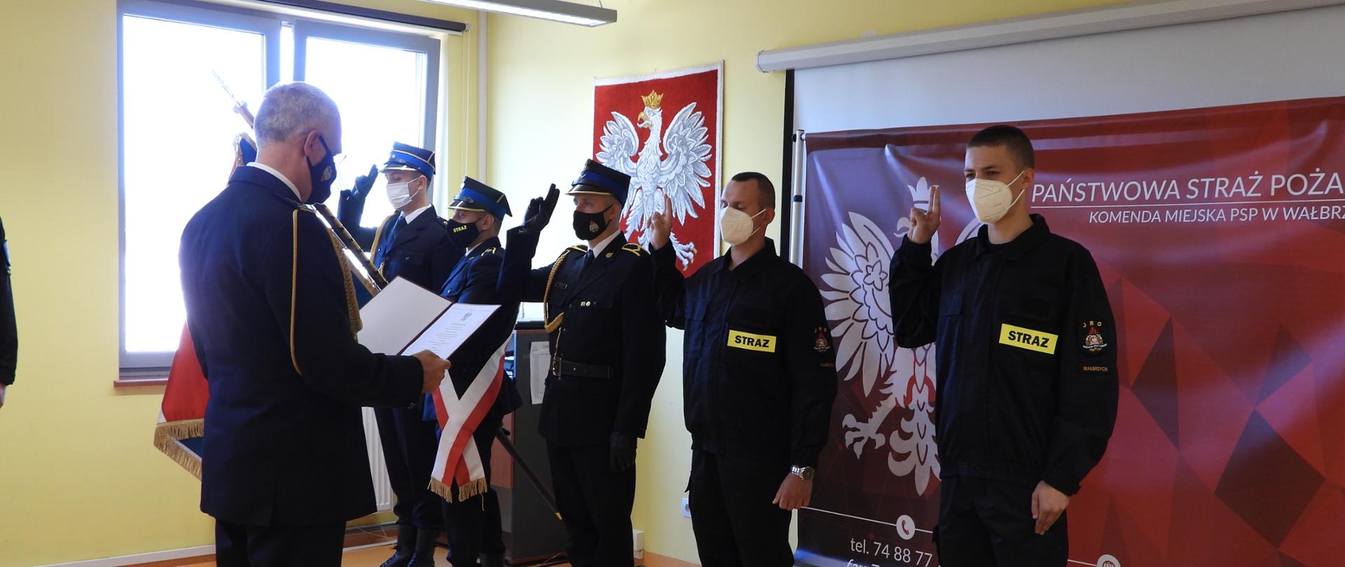 Komendant Miejski PSP w Wałbrzychu czyta tekst ślubowania. Strażacy stojący przed nim mają podniesioną prawą rękę