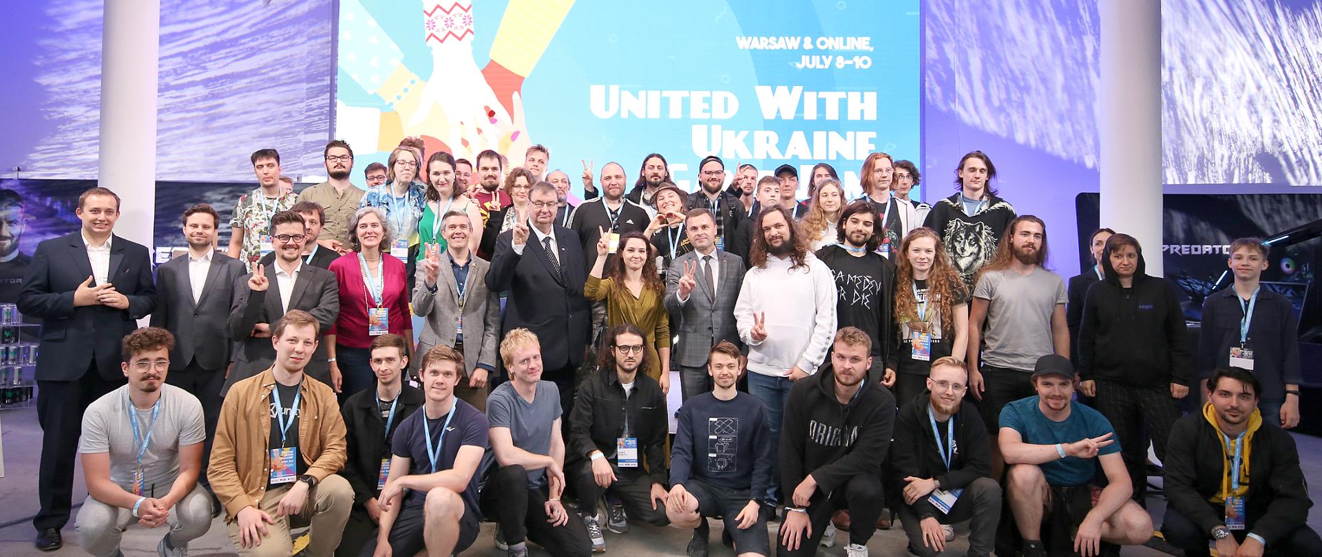 Zdjęcie grupowe z uczestnikami na tle planszy z napisem United with Ukraine game jam