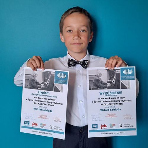 Chłopiec elegancko ubrany trzyma w rękach dwa dyplomy wyróżnienia i dla najmłodszego uczestnika w XIV Konkursie Wiedzy o Życiu i Twórczości Kompozytorów: prof. Józef Świder, Jastrzębie-Zdrój, 22.05.2023 r.