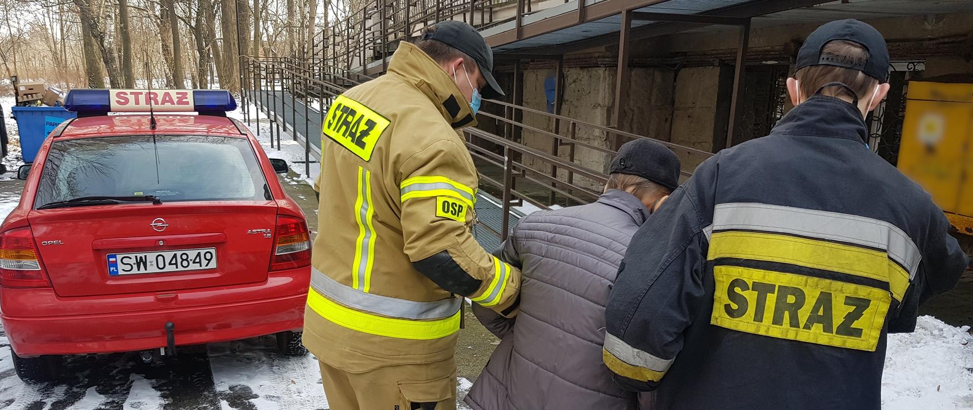 Zdjęcie przedstawia dwóch strażaków pomagających mieszkańcowi Świętochłowic w dotarciu do punktu szczepień.