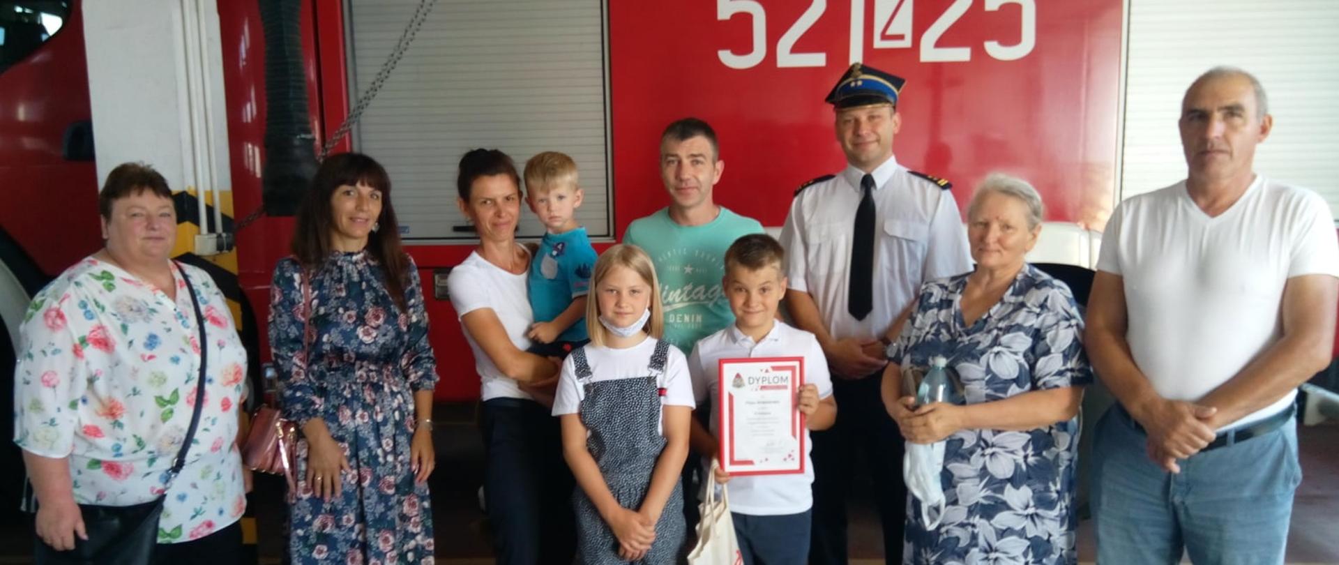 Pamiątkowe zdjęcie na tle samochodu ratowniczo-gaśniczego o numerze operacyjnym 521Z25. Wśród grupy możemy wyróżnić lauerata konkursu oraz bryg. Pawła Faryno, dodatkowo na zdjęciu znajduje się rodzina lauerata oraz jego nauczyciele.