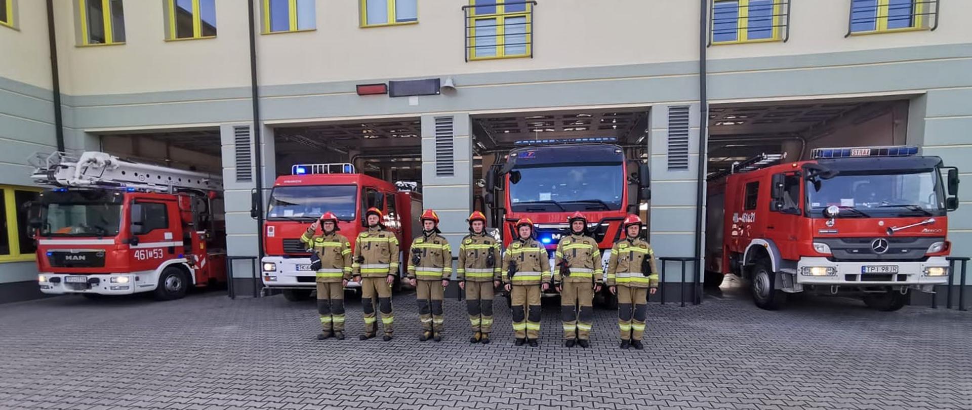 Zdjęcie przedstawia strażaków PSP w umundurowaniu bojowym oddających hołd ofiarom katastrofy smoleńskiej. Za strażakami widać pojazdy pożarnicze z załączonymi sygnałami świetlnymi