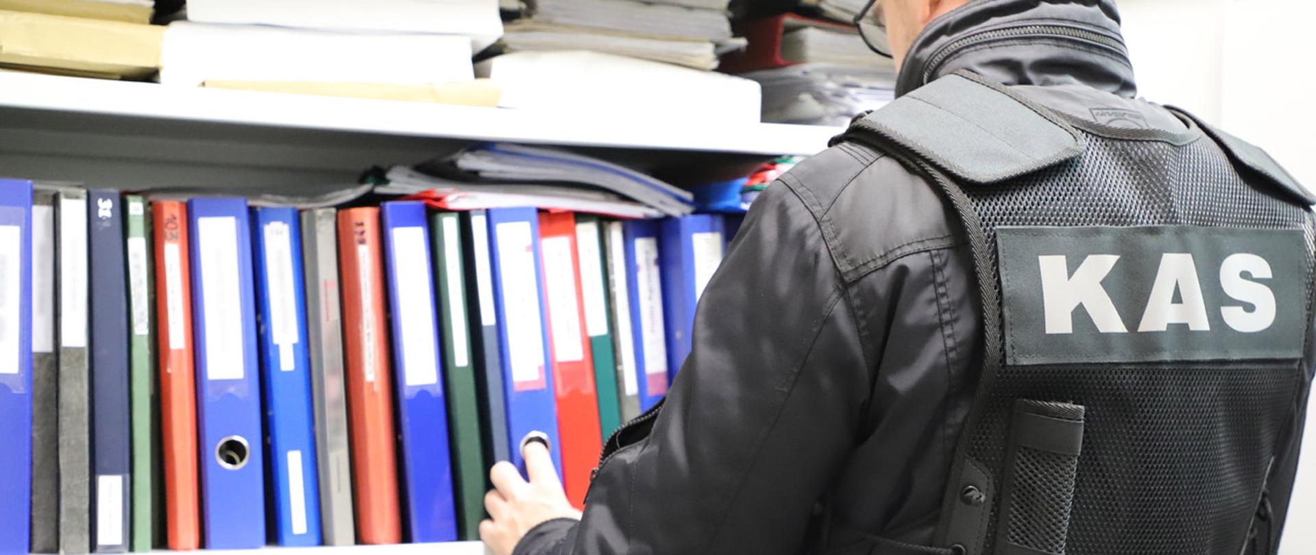 Funkcjonariusz KAS przy regale z segregatorami z dokumentami.