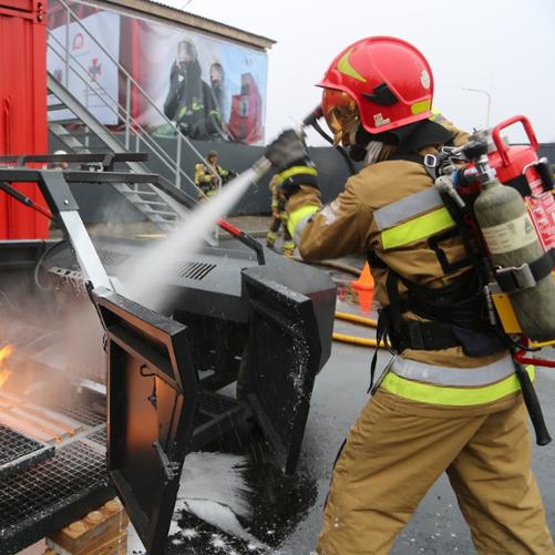 Strażak gasi płonący samochód gaśnicą, w tle logo Polska pomoc