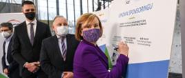 Wiceminister sportu i turystyki Anna Krupka składa autograf na planszy poświęconej podpisaniu umowy sponsoringowej przez PGE Polską Grupę Energetyczną oraz polskie związki łyżwiarskie.