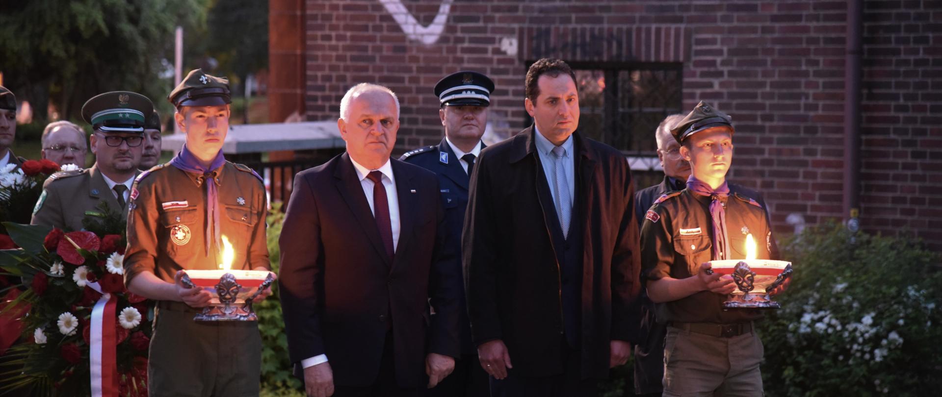 Wojewoda z dyrektorem IPN i harcerzami, którzy trzymają znicze