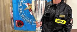 St.sekc. Marian Łazarski trzymający puchar drużynowego Mistrza Polski Komendanta Głównego, w tle sztandar KP PSP w Wąbrzeźnie.