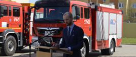 Zdjęcie przedstawia Burmistrza Wałcza przy mównicy na tle samochodów pożarniczych 