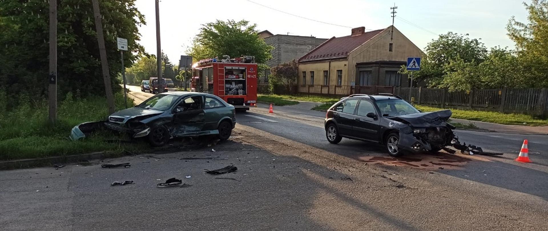 Na zdjęciu widzimy dwa samochody osobowe po kolizji drogowej. Siła zderzenia była tak duża, że auta znajdują się w odległości 5 metrów od siebie. Na ulicy widzimy porozrzucane elementy karoserii. Samochód Opel znajdujący się z lewej strony zdjęcia ma uszkodzony cały bok od strony kierowcy. Samochód Rover znajdujący się z prawej strony zdjęcia ma uszkodzony przód pojazdu. Z samochodu Rover na pas jezdni wyciekły płyny eksploatacyjne, które zostały zneutralizowane przez strażaków za pomocą sorbentu Compact. W obu pojazdach podniesiono klapy od silnika w celu odłączenia akumulatorów.